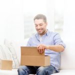 A man sitting on a couch opening a box.