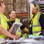 Three DHL employees are having a conversation in a warehouse.